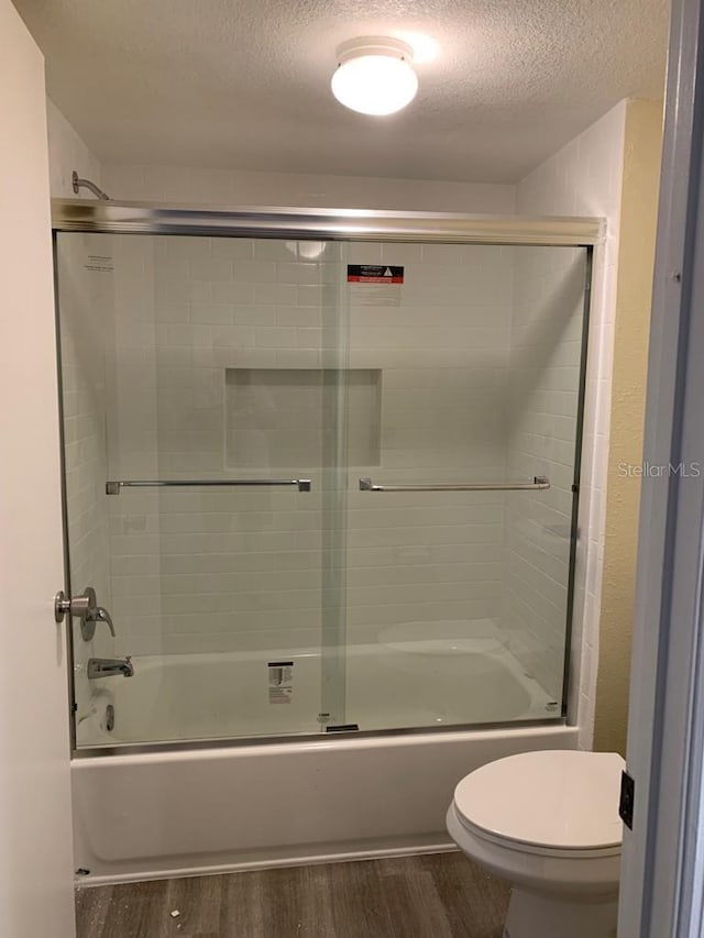 bathroom with hardwood / wood-style flooring, enclosed tub / shower combo, a textured ceiling, and toilet