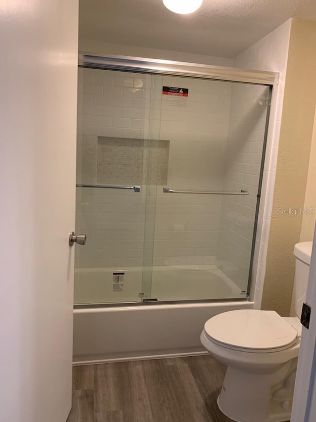 bathroom with hardwood / wood-style flooring, bath / shower combo with glass door, toilet, and a textured ceiling