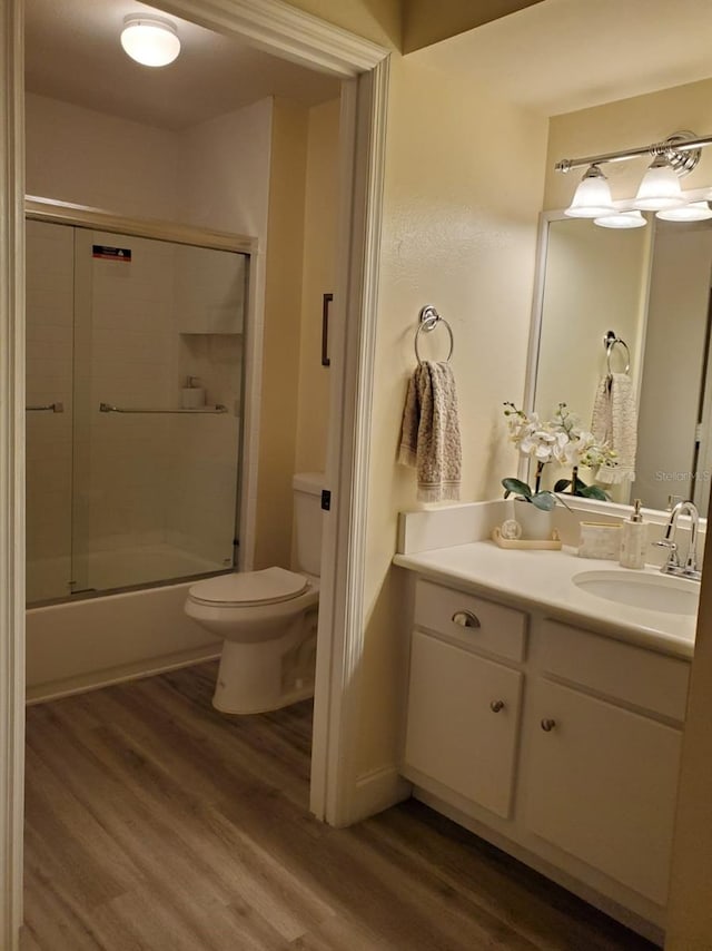 full bathroom featuring vanity, combined bath / shower with glass door, hardwood / wood-style floors, and toilet