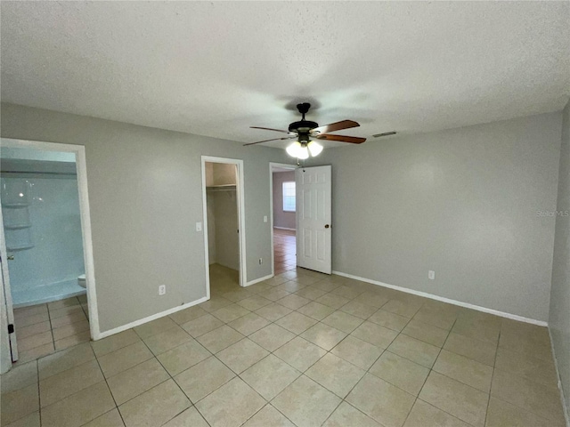 unfurnished bedroom with ceiling fan, a textured ceiling, light tile patterned flooring, a spacious closet, and a closet