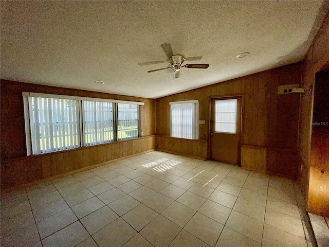 tiled spare room featuring ceiling fan, lofted ceiling, a textured ceiling, and wood walls