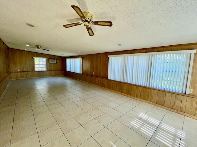 spare room featuring light tile patterned floors, ceiling fan, a textured ceiling, and wood walls