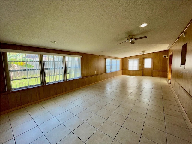 tiled empty room featuring ceiling fan, a textured ceiling, and wooden walls