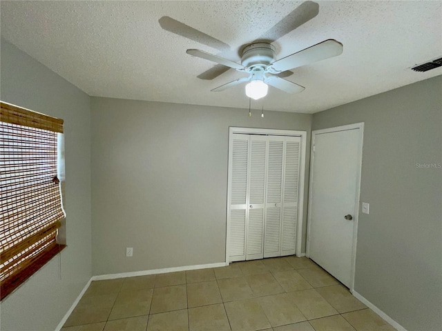 unfurnished bedroom featuring light tile patterned flooring, ceiling fan, a textured ceiling, and a closet