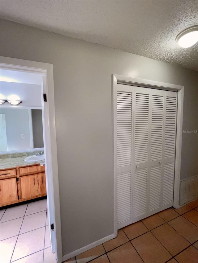 hall with sink, a textured ceiling, and light tile patterned floors