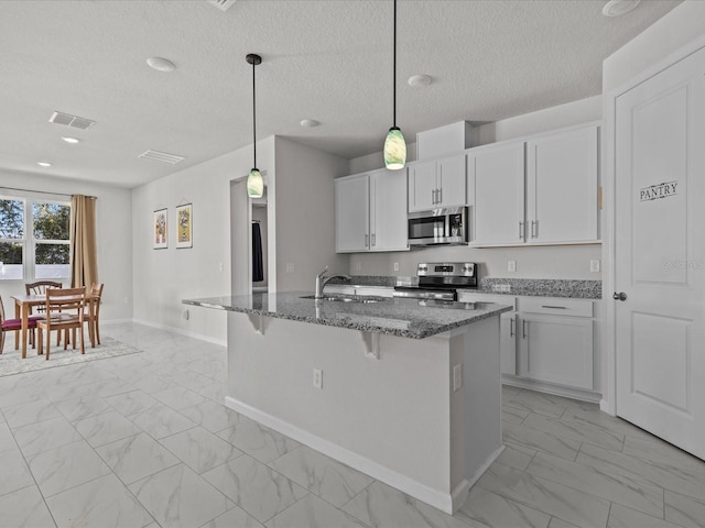 kitchen featuring sink, white cabinetry, decorative light fixtures, appliances with stainless steel finishes, and a kitchen island with sink