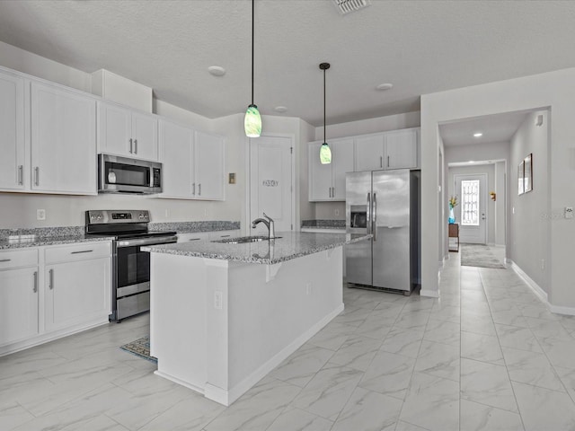 kitchen with appliances with stainless steel finishes, white cabinetry, an island with sink, sink, and light stone countertops