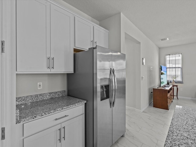 kitchen featuring white cabinetry, light stone countertops, stainless steel fridge, and a textured ceiling