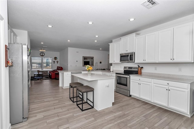 kitchen with a breakfast bar area, a center island, kitchen peninsula, stainless steel appliances, and white cabinets