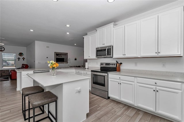 kitchen with white cabinetry, a kitchen breakfast bar, a center island, kitchen peninsula, and stainless steel appliances