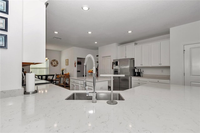 kitchen with light stone counters, sink, white cabinetry, and stainless steel fridge