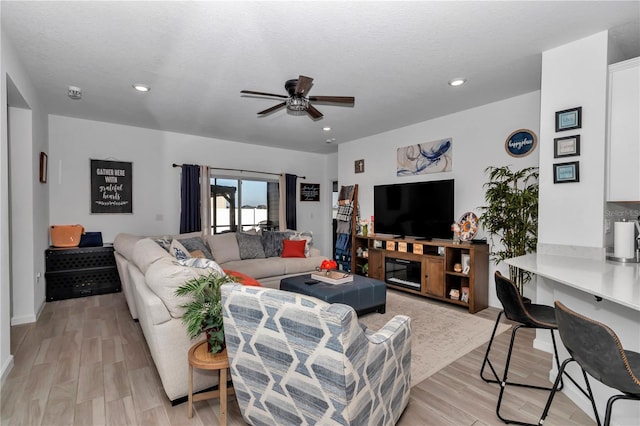 living room with ceiling fan, a textured ceiling, and light hardwood / wood-style floors