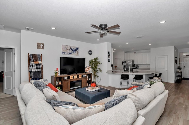 living room with ceiling fan, a textured ceiling, and light wood-type flooring