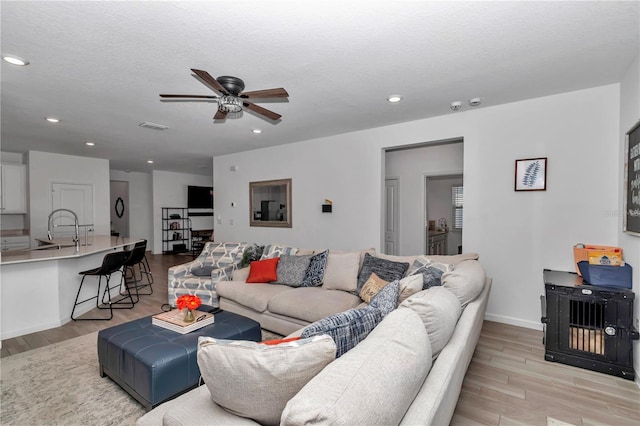 living room featuring ceiling fan, light hardwood / wood-style floors, sink, and a textured ceiling