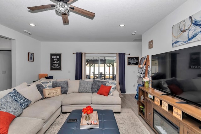 living room featuring ceiling fan, a textured ceiling, and light wood-type flooring