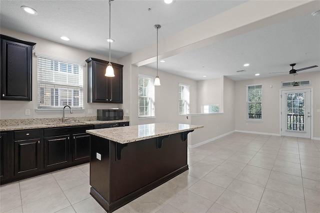 kitchen with sink, a breakfast bar area, a center island, hanging light fixtures, and light tile patterned floors