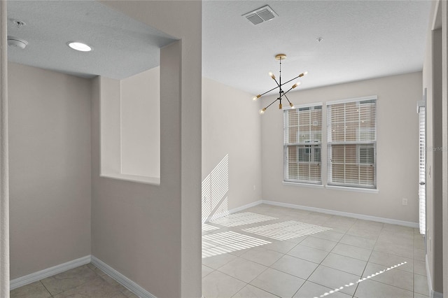 spare room featuring a notable chandelier, a textured ceiling, and light tile patterned floors