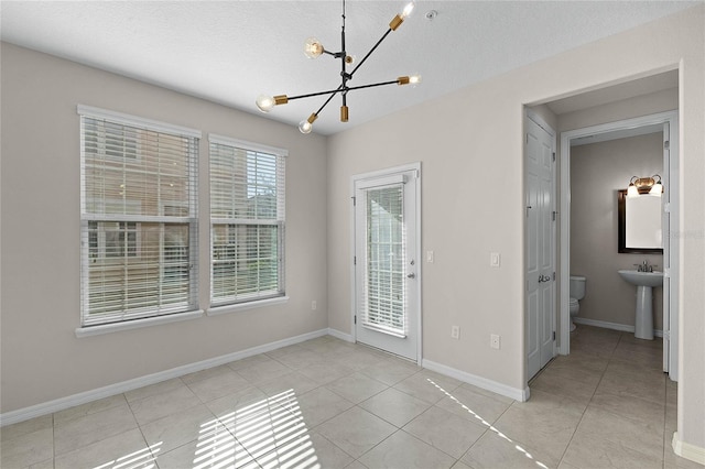 tiled empty room with an inviting chandelier, sink, and a textured ceiling