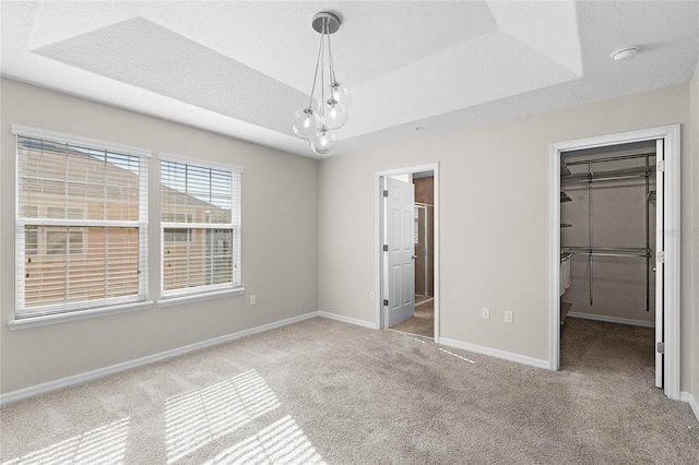 unfurnished bedroom with a walk in closet, light carpet, a textured ceiling, a tray ceiling, and a closet