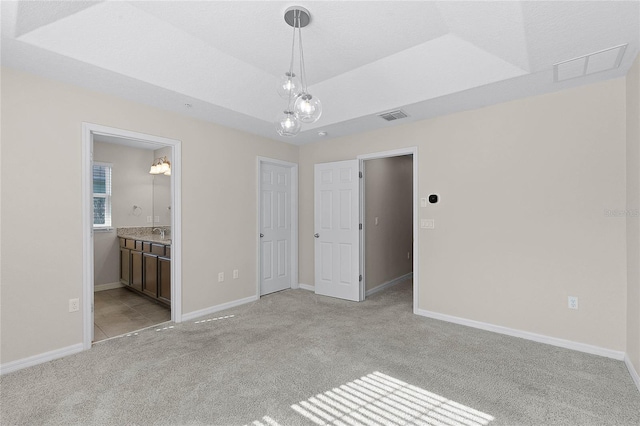 unfurnished bedroom with connected bathroom, sink, light carpet, and a tray ceiling