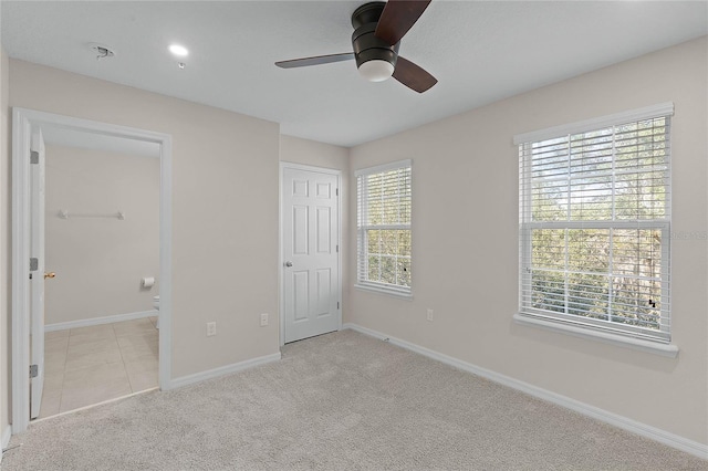 unfurnished bedroom featuring multiple windows, ceiling fan, light carpet, and ensuite bath