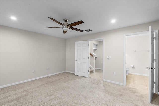 unfurnished bedroom featuring ensuite bath, a walk in closet, light colored carpet, and ceiling fan