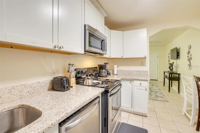 kitchen featuring white cabinetry, appliances with stainless steel finishes, light tile patterned floors, and light stone counters