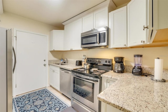 kitchen with light tile patterned floors, sink, stainless steel appliances, light stone countertops, and white cabinets