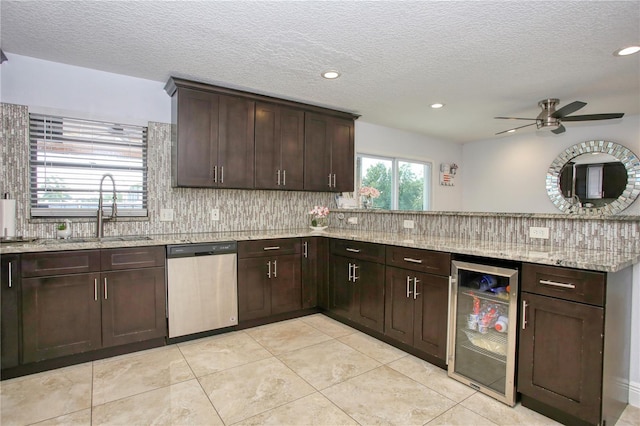 kitchen featuring dark brown cabinetry, sink, dishwasher, beverage cooler, and light stone countertops