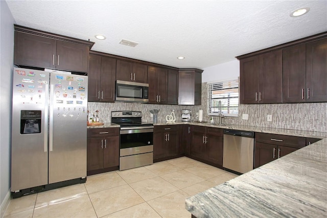 kitchen featuring tasteful backsplash, light tile patterned floors, light stone counters, stainless steel appliances, and dark brown cabinets