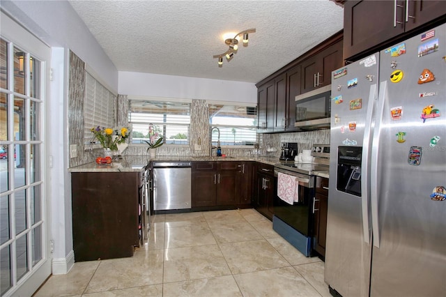 kitchen with appliances with stainless steel finishes, sink, decorative backsplash, light stone counters, and dark brown cabinetry