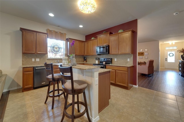 kitchen with a kitchen bar, dishwasher, a kitchen island, electric stove, and backsplash