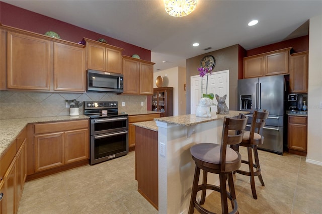 kitchen with light stone countertops, a breakfast bar area, stainless steel appliances, and a center island