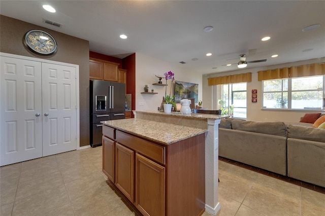 kitchen with light stone countertops, a center island, high end fridge, and light tile patterned floors