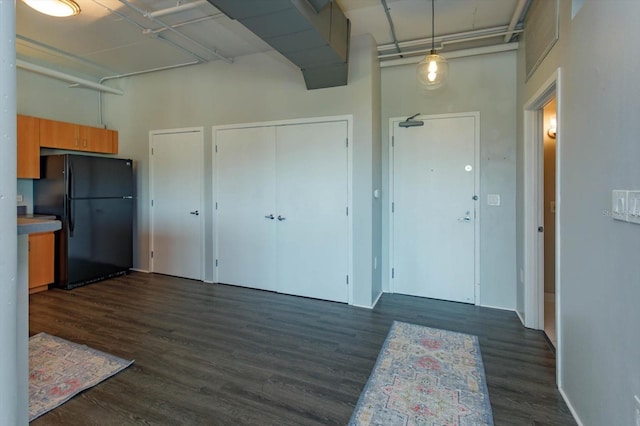 kitchen with black fridge, a towering ceiling, and dark wood-type flooring