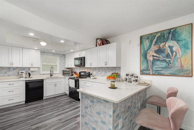 kitchen with sink, white cabinetry, black appliances, a kitchen bar, and kitchen peninsula