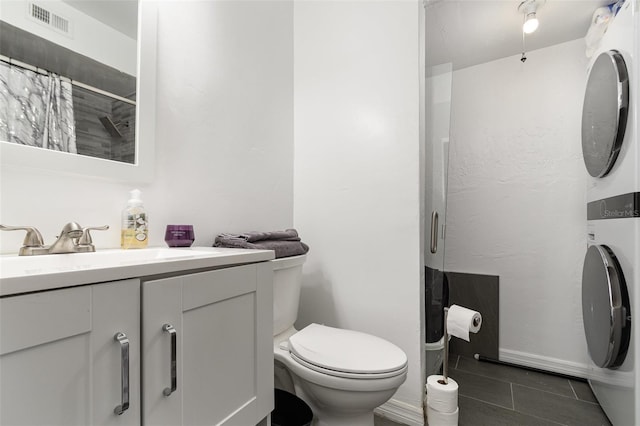 bathroom featuring toilet, a shower with curtain, vanity, stacked washer / dryer, and tile patterned flooring