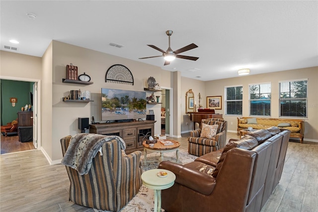 living room featuring ceiling fan, a fireplace, and light wood-type flooring