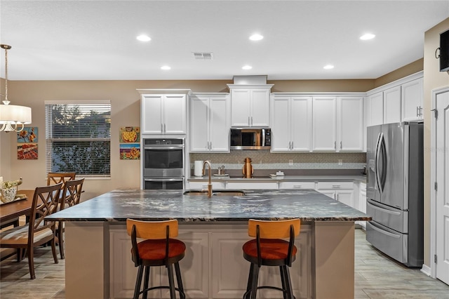 kitchen featuring pendant lighting, white cabinetry, appliances with stainless steel finishes, and a center island with sink