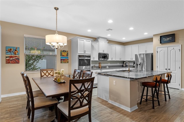 kitchen with pendant lighting, white cabinets, dark stone counters, stainless steel appliances, and a center island with sink