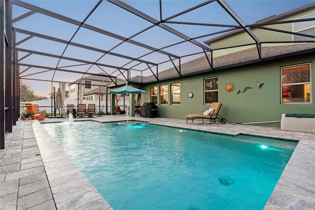 pool at dusk with a patio, a lanai, and pool water feature