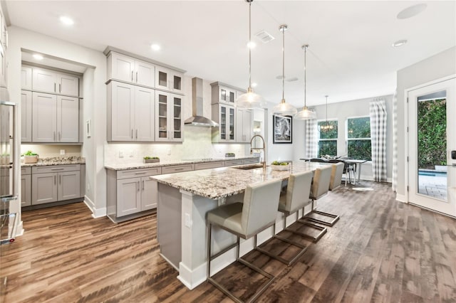 kitchen featuring an island with sink, sink, a breakfast bar area, gray cabinetry, and wall chimney range hood