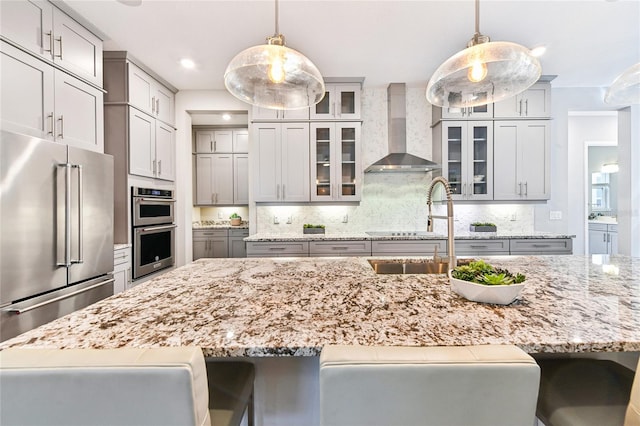 kitchen with gray cabinetry, wall chimney range hood, stainless steel appliances, and hanging light fixtures