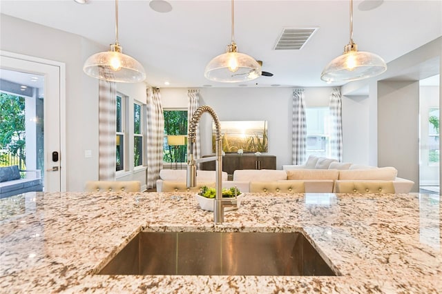 kitchen with light stone counters, sink, and hanging light fixtures