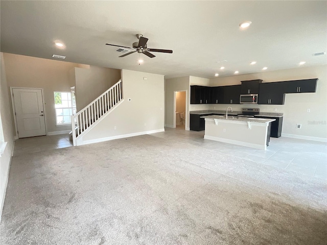 kitchen with appliances with stainless steel finishes, a kitchen island with sink, sink, and light colored carpet