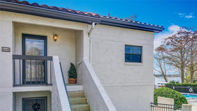 property entrance featuring a tile roof, fence, and stucco siding