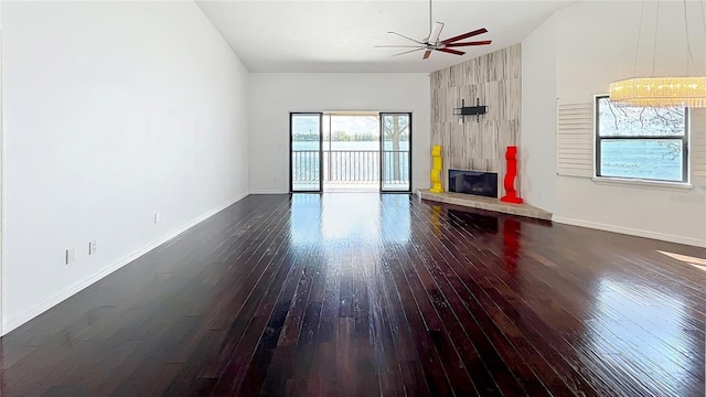 unfurnished living room with hardwood / wood-style flooring, a ceiling fan, baseboards, vaulted ceiling, and a tiled fireplace