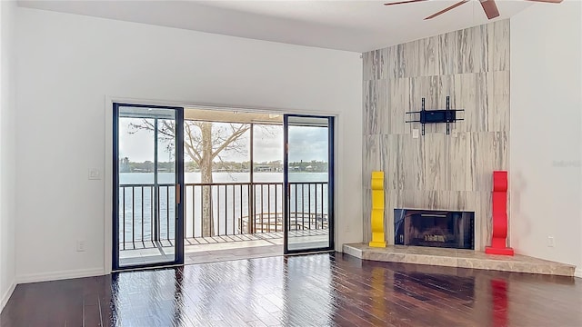 unfurnished living room featuring ceiling fan, wood finished floors, a water view, and a tile fireplace