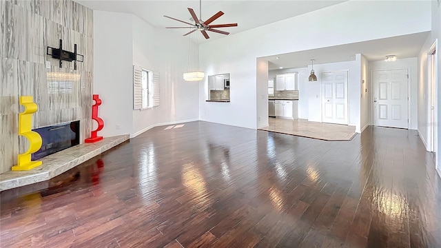 unfurnished living room featuring baseboards, a ceiling fan, a towering ceiling, dark wood-type flooring, and a fireplace