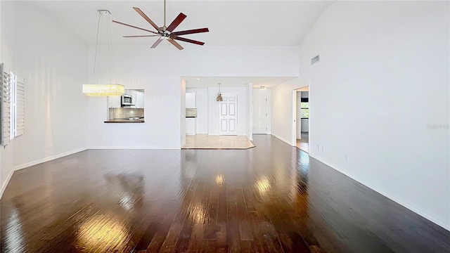 unfurnished living room featuring a towering ceiling, baseboards, visible vents, a ceiling fan, and dark wood-style floors